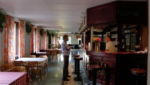 A restaurant with a bar area, tables, and chairs arranged for dining.