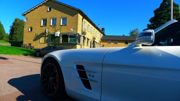 A white sports car parked in front of a building with a sign that reads "RUM."