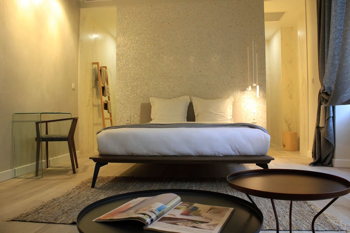 A modern bedroom with a bed, bedside tables, a glass chair, and a magazine on the floor.