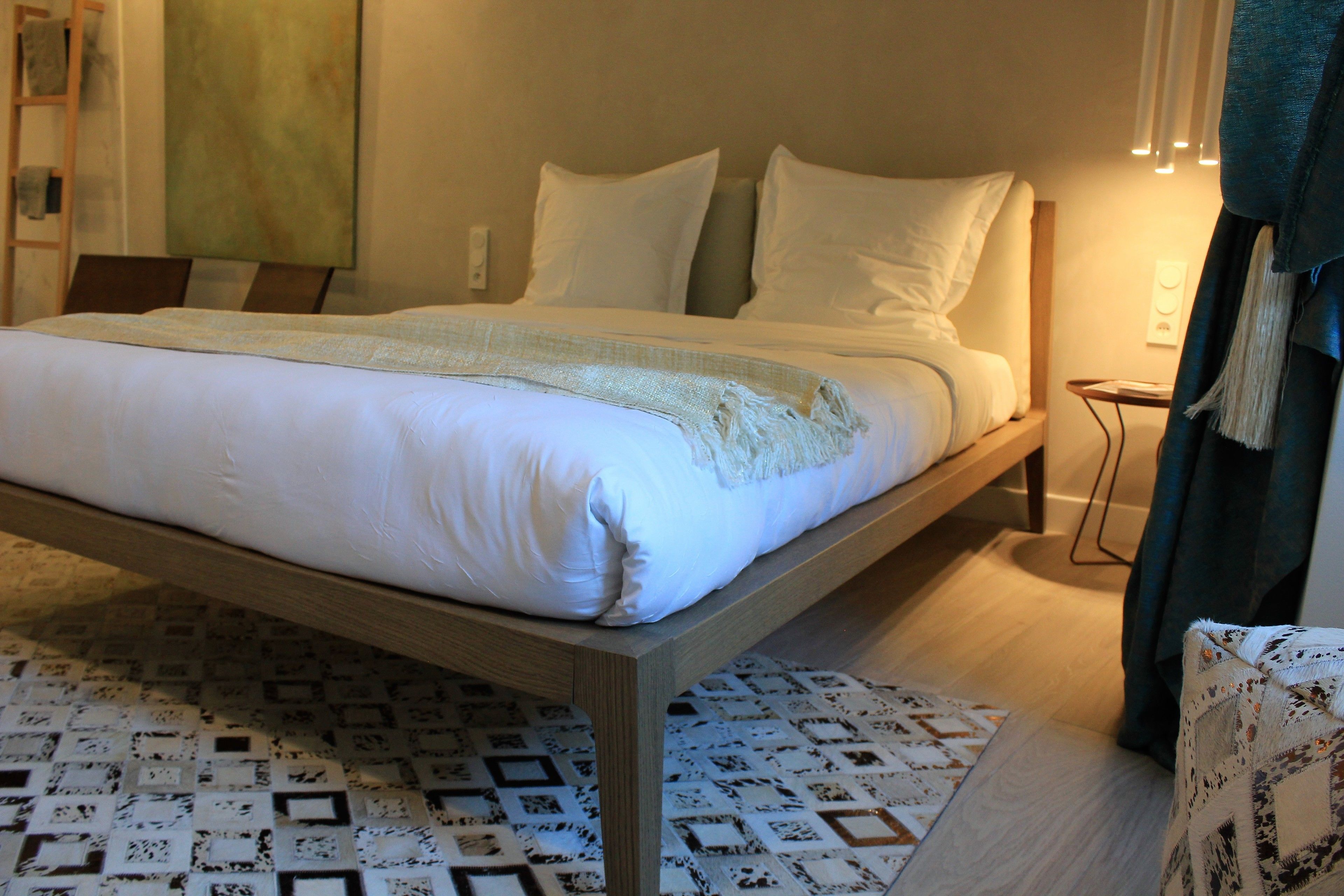 A bed with a wooden frame, white bedding, and a patterned rug.