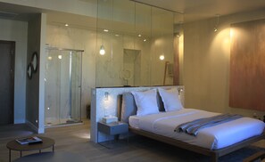 Ein modernes Schlafzimmer mit einem großen Bett, einem Nachttisch, einer kleinen runden Spiegel und einer Duschkabine aus Glas.