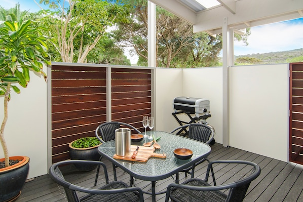 An outdoor patio with a glass table, black wicker chairs, a grill, and potted plants. - Margaret River Beach Studios (Prevelly)