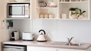 Una cocina compacta con armarios blancos, microondas integrado, tostadora, hervidor y lavavajillas.