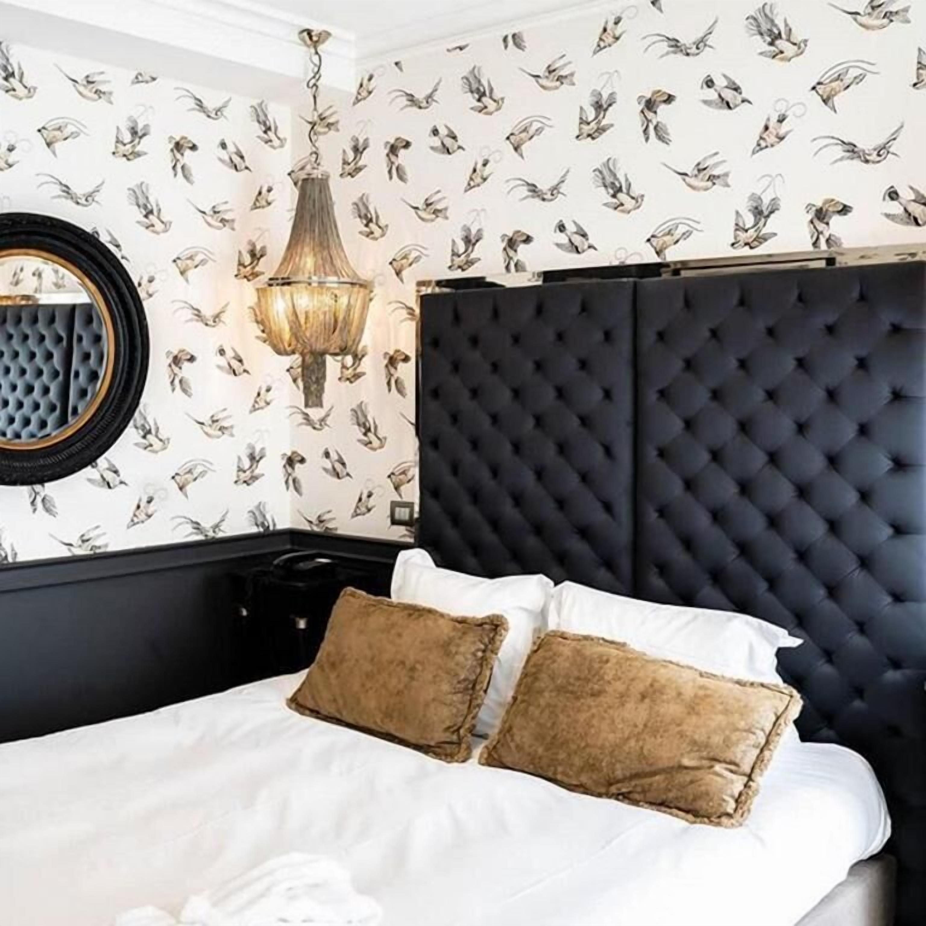 A bedroom with a tufted headboard, a round mirror, and patterned wallpaper.