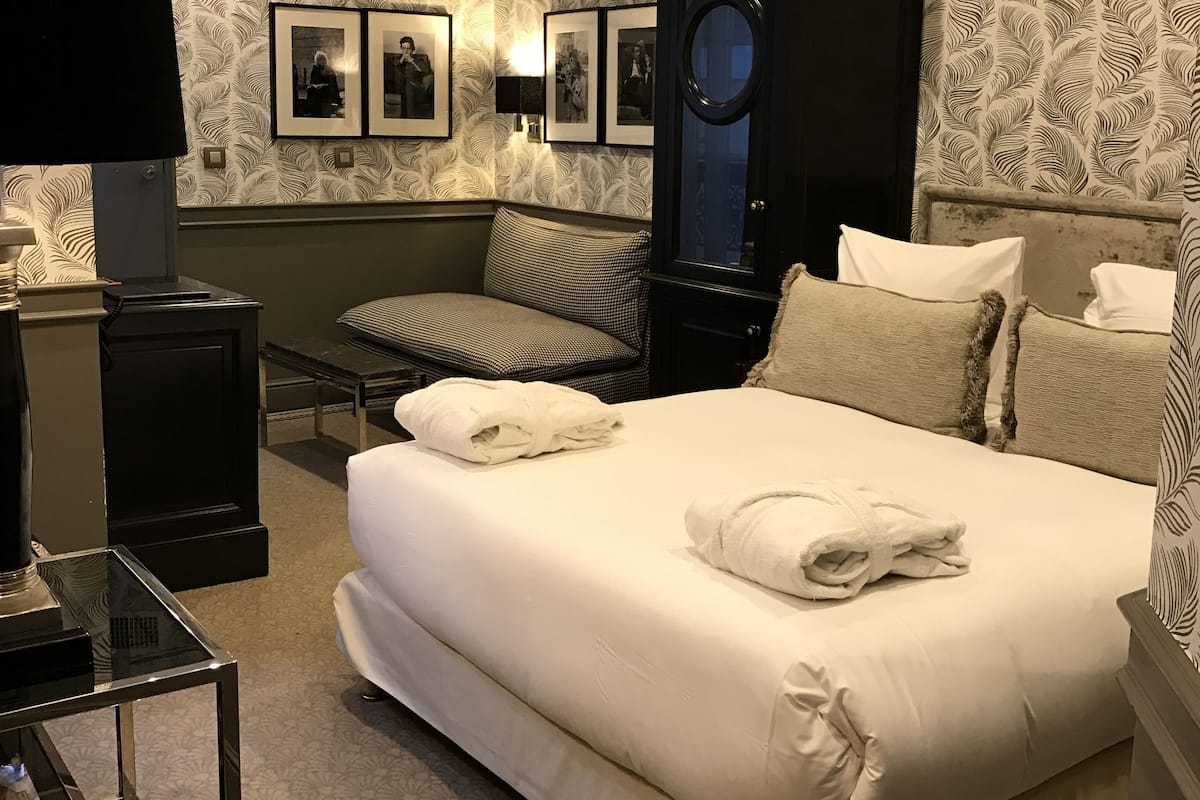 A hotel room with a large bed, a dark cabinet, a desk with a lamp, and patterned wallpaper.