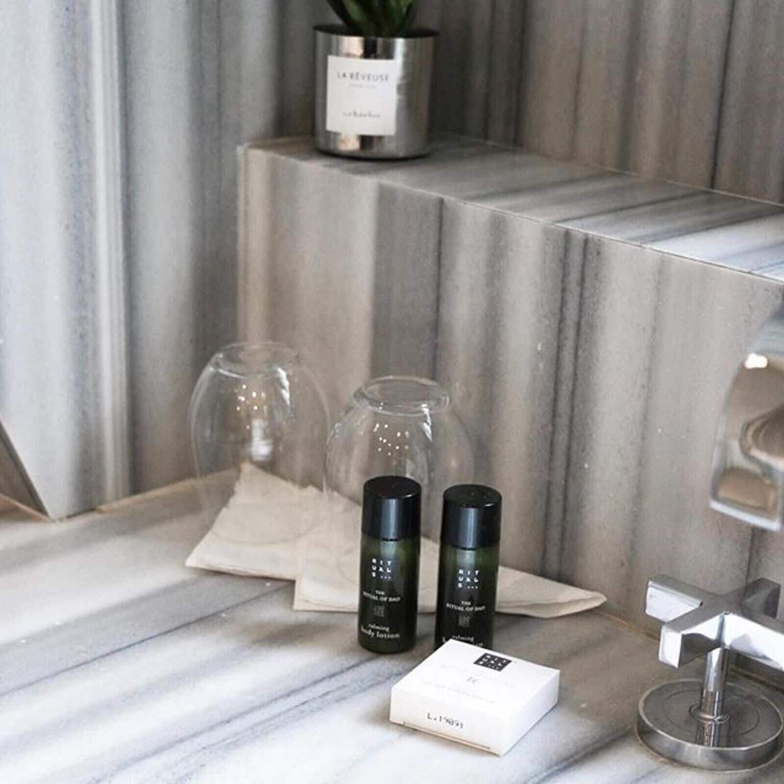 A bathroom vanity with a marble countertop, two black bottles of lotion, a white box, and a potted plant.