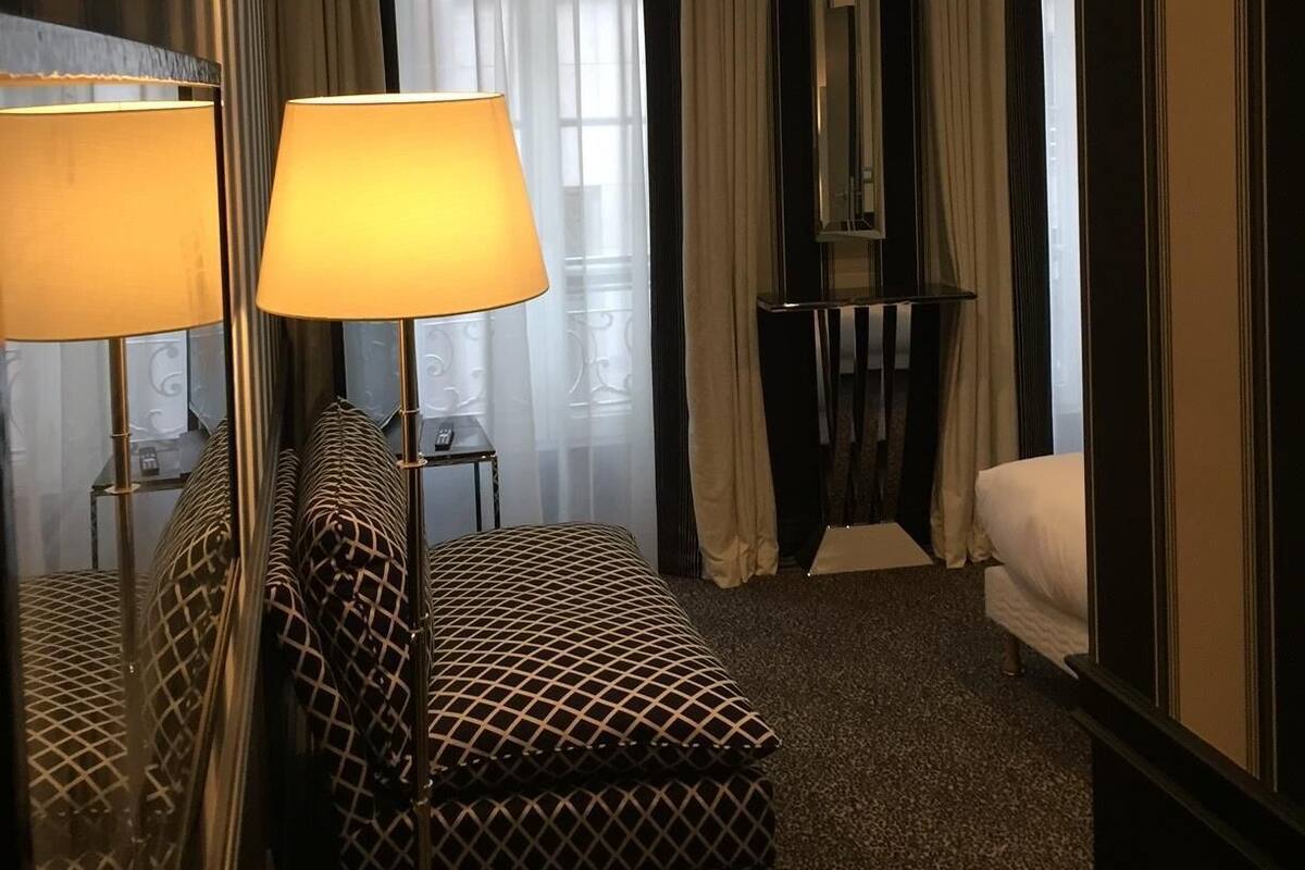 A hotel room with a bed, a sofa, a standing lamp, and a mirror.