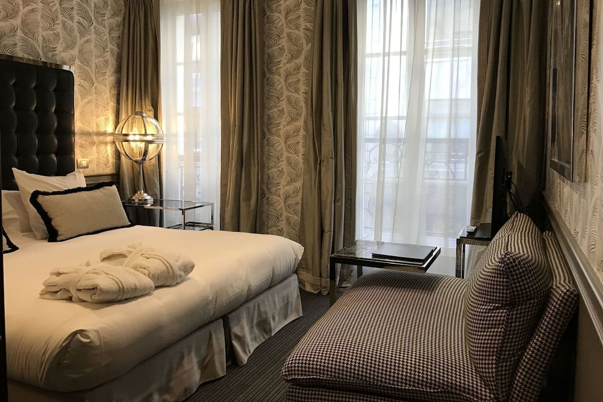 A hotel room with a large bed, a sofa, a small table, a lamp, and a TV.
