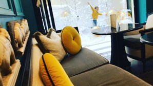 Un salón moderno con un sofá, cojines amarillos y vistas a una persona con una camiseta amarilla en el exterior.