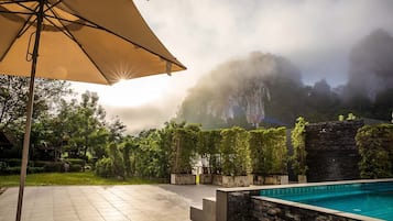 Un área de piscina con un muro de piedra y una sombrilla grande.