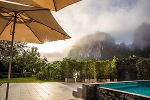 Un área de piscina con un muro de piedra y una sombrilla grande.