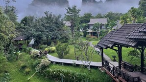 A lush garden with a wooden deck and a gazebo, surrounded by greenery and traditional buildings. - Montania Lifestyle Hotel (Phanom)