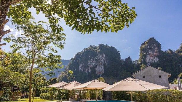 A pool area with lounge chairs and umbrellas, surrounded by lush greenery and overlooking a mountainous landscape. - Montania Lifestyle Hotel (Phanom)