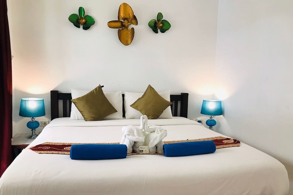 Una cama bien hecha con sábanas blancas, dos almohadones azules y una decoración de toallas.