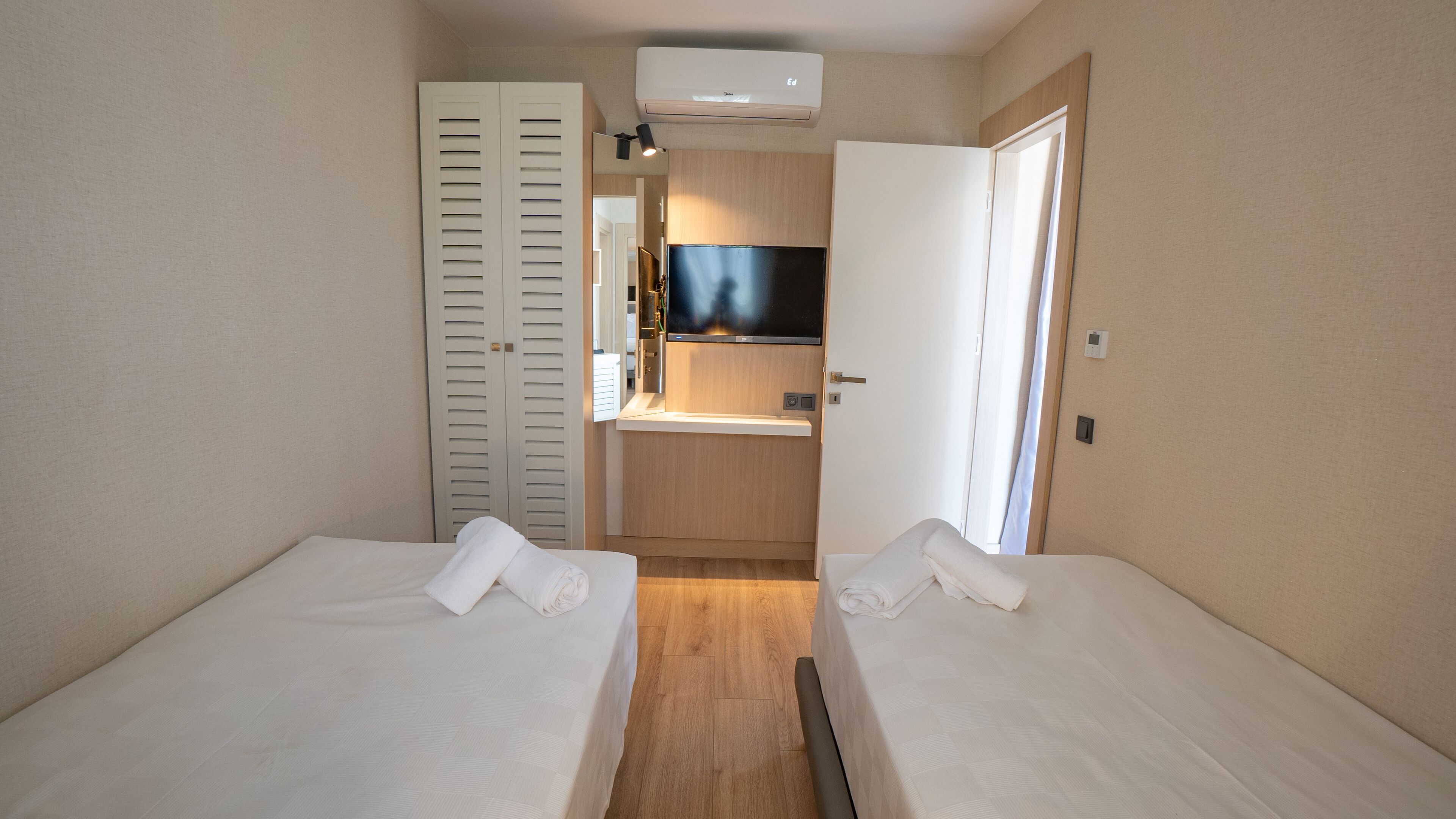 A hotel room with two beds, a small kitchenette, a TV, and a closet.
