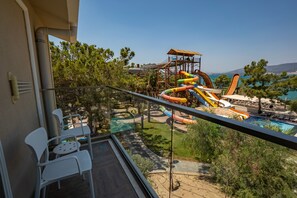 A balcony with white chairs, a pool, and a water park with slides. - Long Beach Club Nature (Didim)