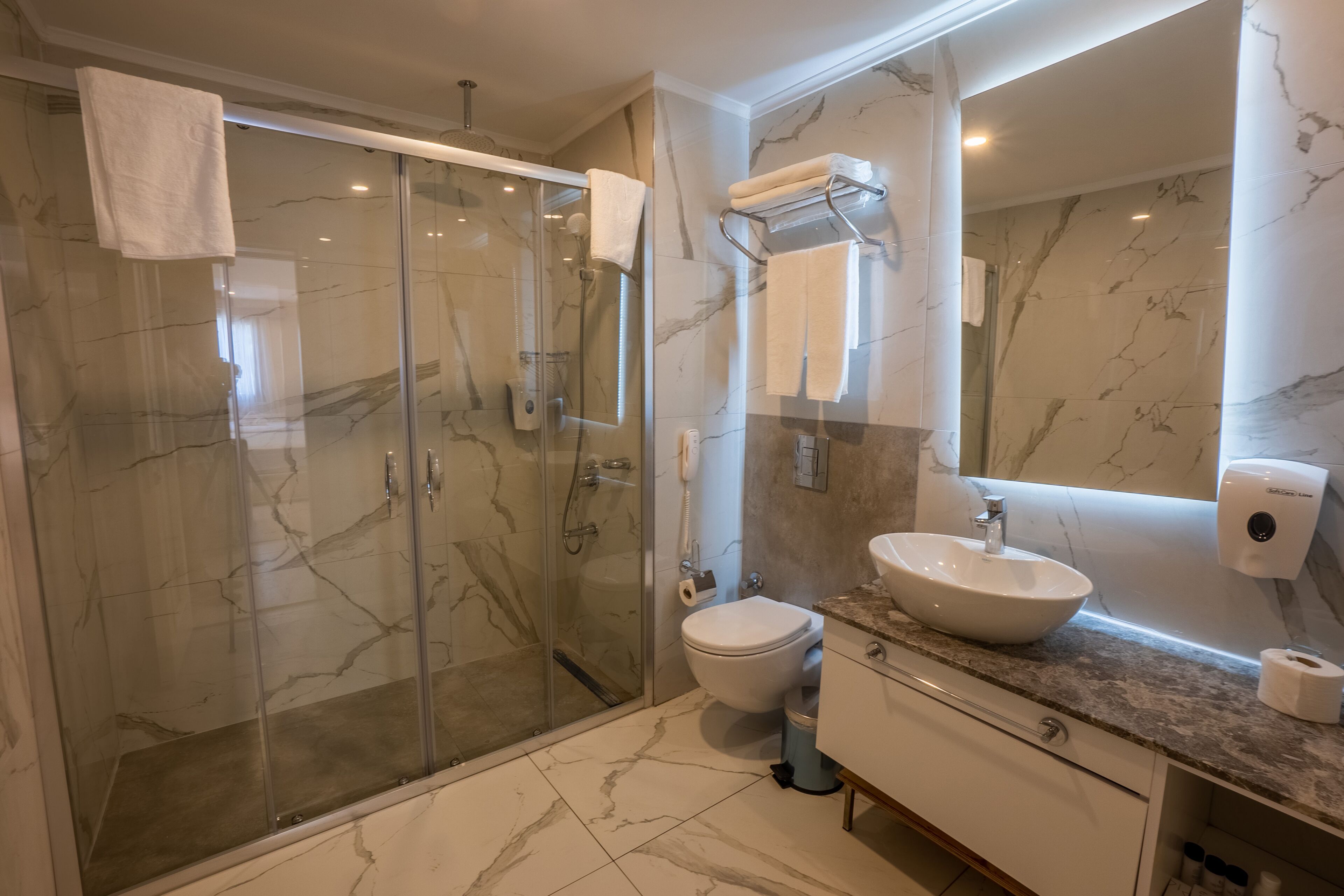 A modern bathroom with a glass-enclosed shower, a white sink, and a marble-tiled floor.
