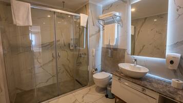 A modern bathroom with a glass-enclosed shower, a white sink, and a marble-tiled floor.
