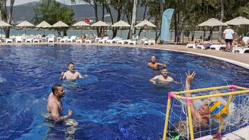 Una piscina con sillones de descanso y sombrillas, rodeada de árboles y vistas al mar.