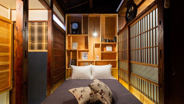 A traditional Japanese-style room with tatami flooring, a bed with a striped bedspread, and a shoji screen door.