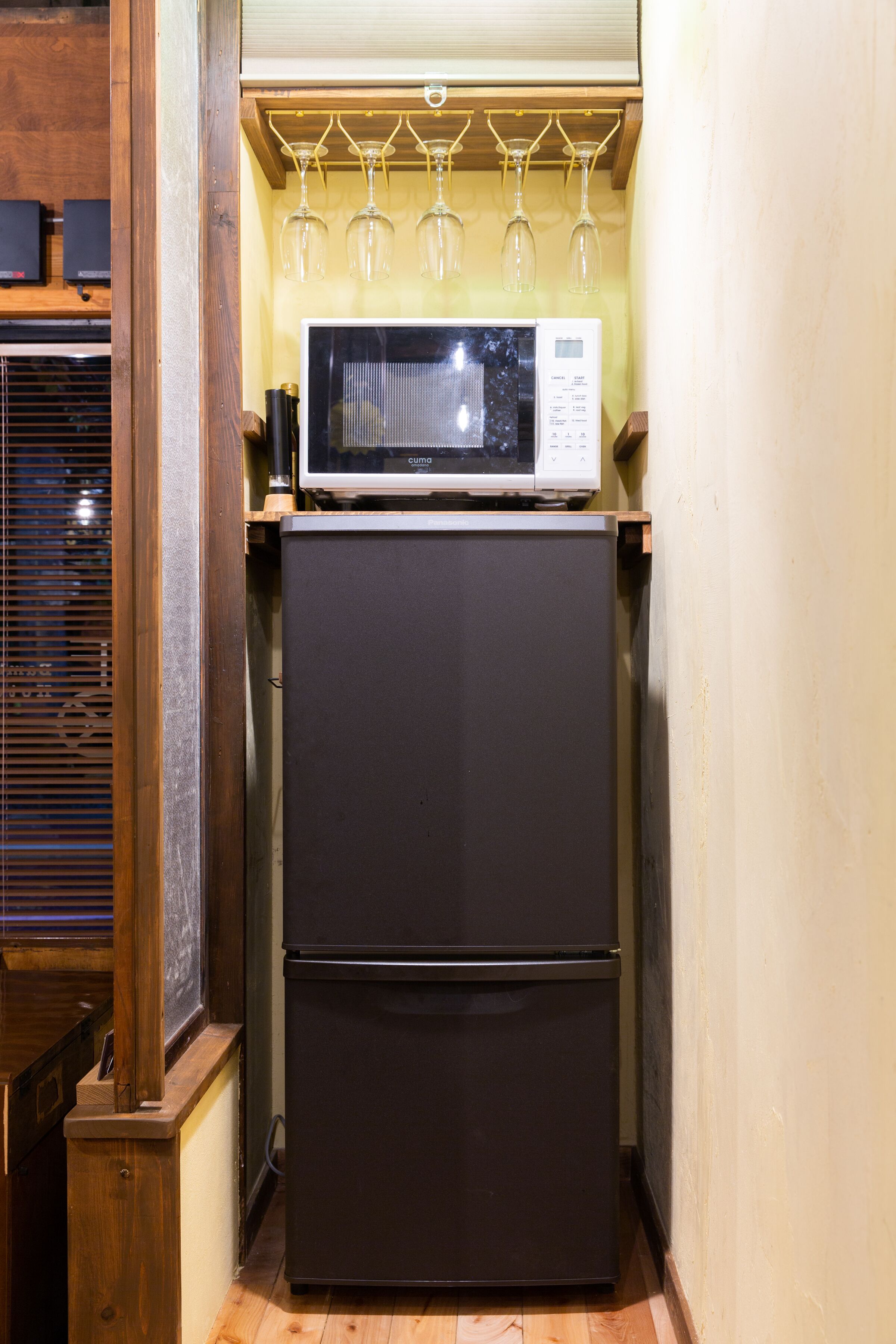 A compact kitchen with a black refrigerator, a microwave, and wine glasses on a shelf.