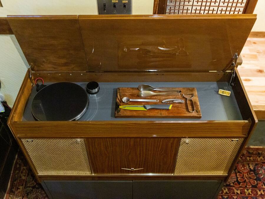 A wooden chest with a hinged lid, containing a black pot, a metal container, and a wooden tray with kitchen utensils.