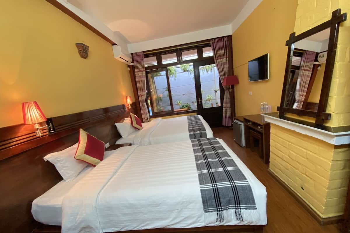 Een hotelkamer met twee bedden, een bureau, een televisie en een raam met gordijnen.