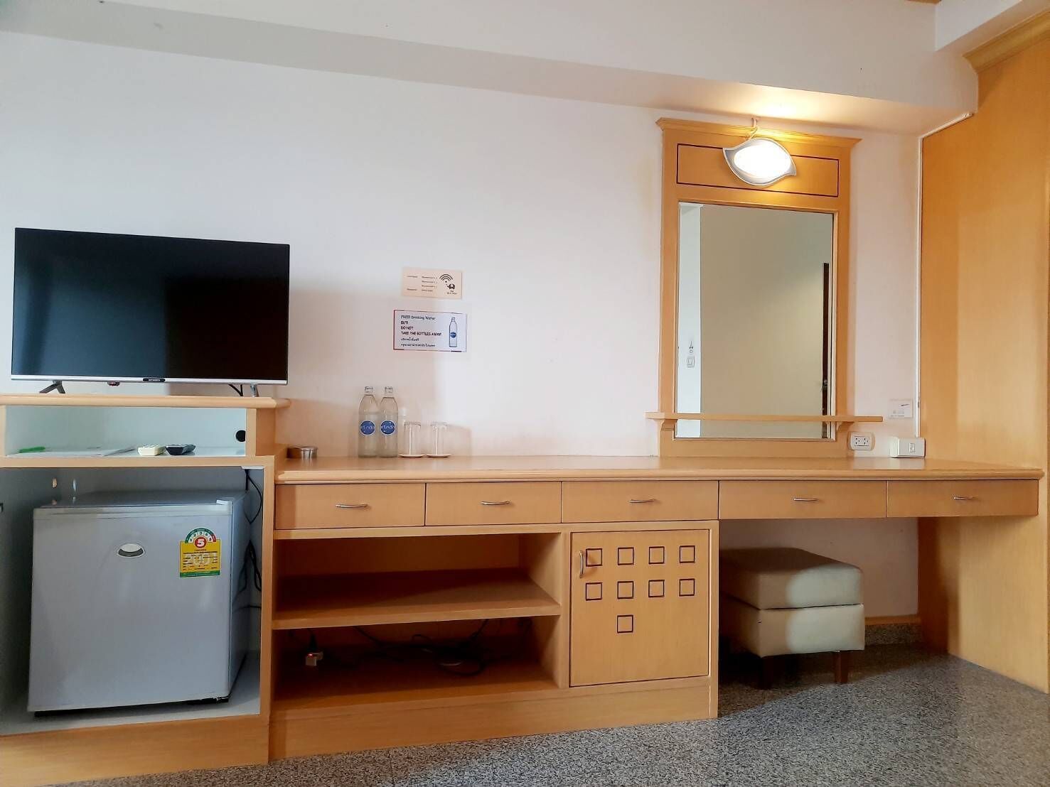 Een compacte hotelkamer met een televisie, een kleine koelkast, een spiegel en een bureau met lades.