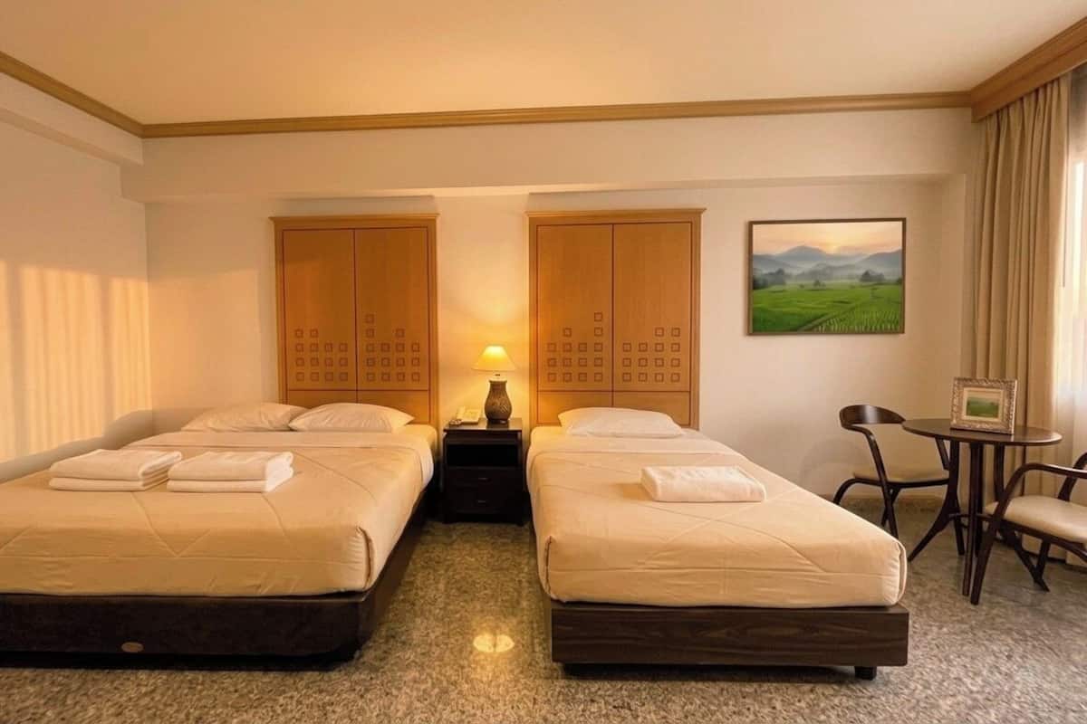 A hotel room with two beds, a desk, a chair, a lamp, and a painting on the wall.