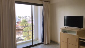 A room with a large window, a flat-screen TV on a wooden stand, and a small cabinet. - Maneerote Hotel Surin (Surin)