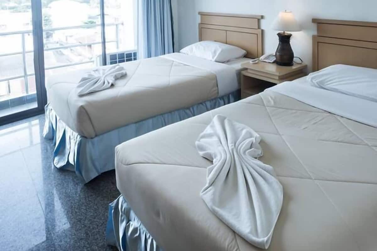 A hotel room with two beds, a nightstand with a lamp, and a large window with curtains.