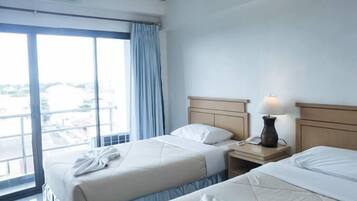 A hotel room with two beds, a nightstand with a lamp, and a large window with curtains.