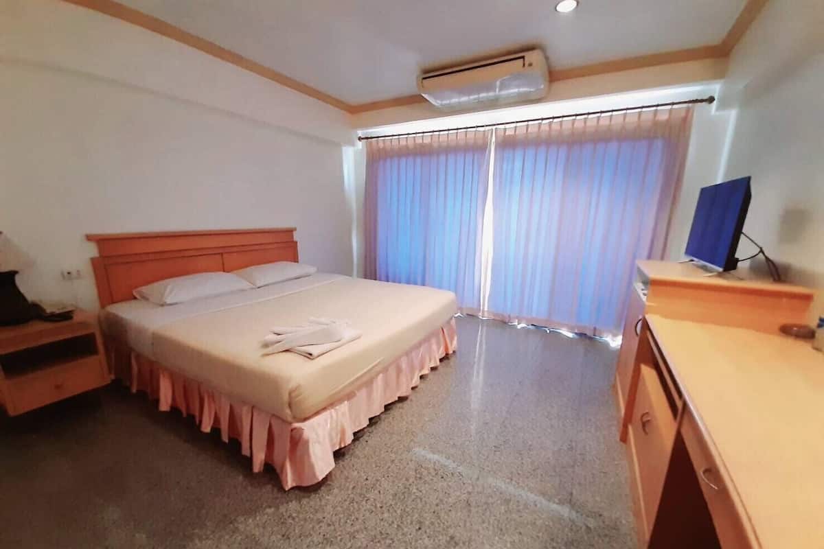 A bedroom with a bed, a desk, an air conditioner, and a window with curtains.