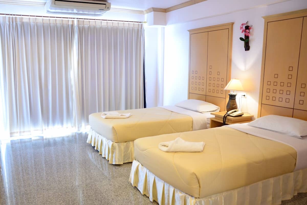 A hotel room with two beds, a large window with curtains, an air conditioning unit, a nightstand with a lamp, and a wall-mounted telephone.