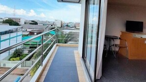 A balcony with a view of the cityscape, a small desk with a chair, and a large window. - Maneerote Hotel Surin (Surin)