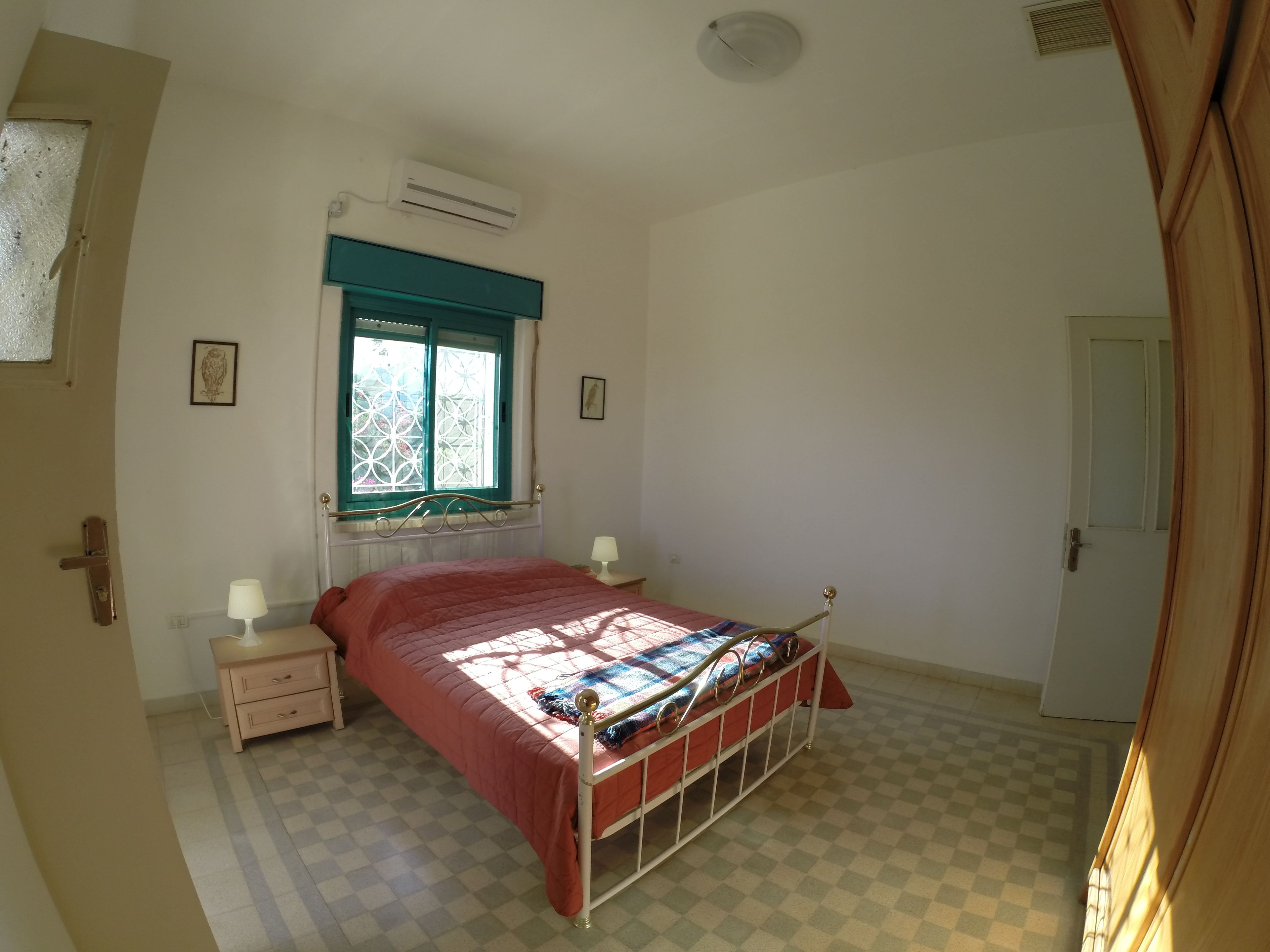 Una camera da letto con un letto, una finestra con cornice blu, un comodino con una lampada e una porta.
