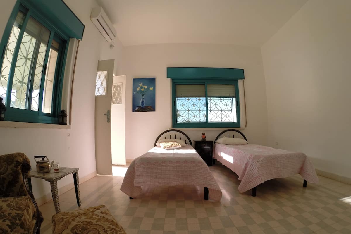 Ein Schlafzimmer mit zwei Betten, einem kleinen Tisch mit Wasserkocher und einem Sessel.