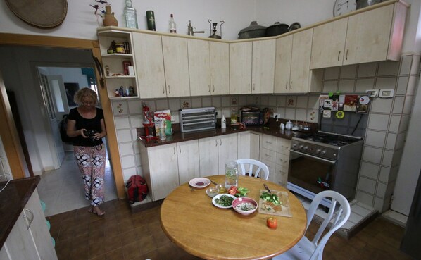 Une cuisine équipée d’une cuisinière, d’un four et de divers appareils électroménagers. On y trouve une table à manger avec des assiettes et une pomme rouge.