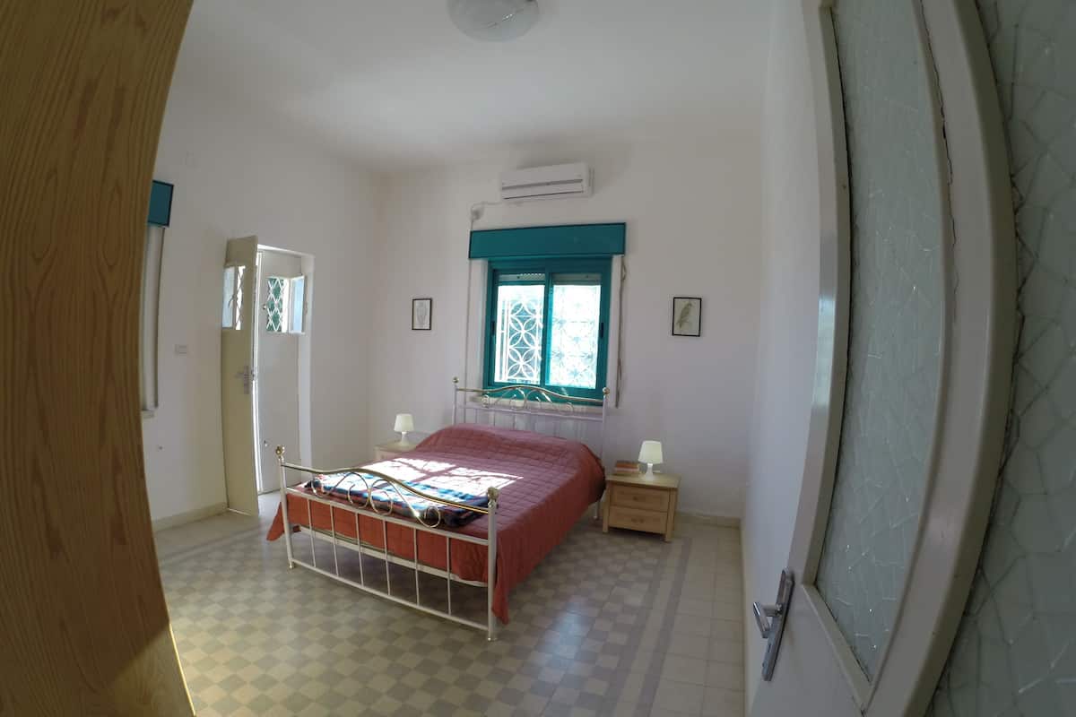 Ein Schlafzimmer mit Bett, einem Fenster mit blauer Vorhangblende, einem Nachttisch mit Lampe und einer Tür.
