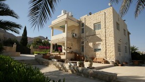 A two-story building with a stone facade, outdoor seating area, and a view of mountains in the background. - Auberg-Inn Guesthouse (Jericho)