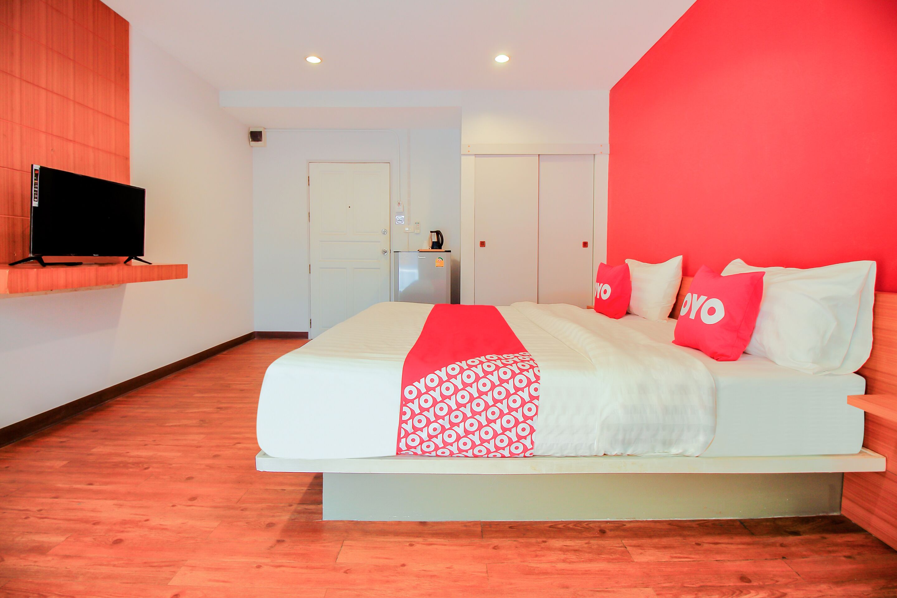 Une chambre d’hôtel moderne avec un lit, un téléviseur posé sur une étagère et un mur d’accent de couleur rouge.