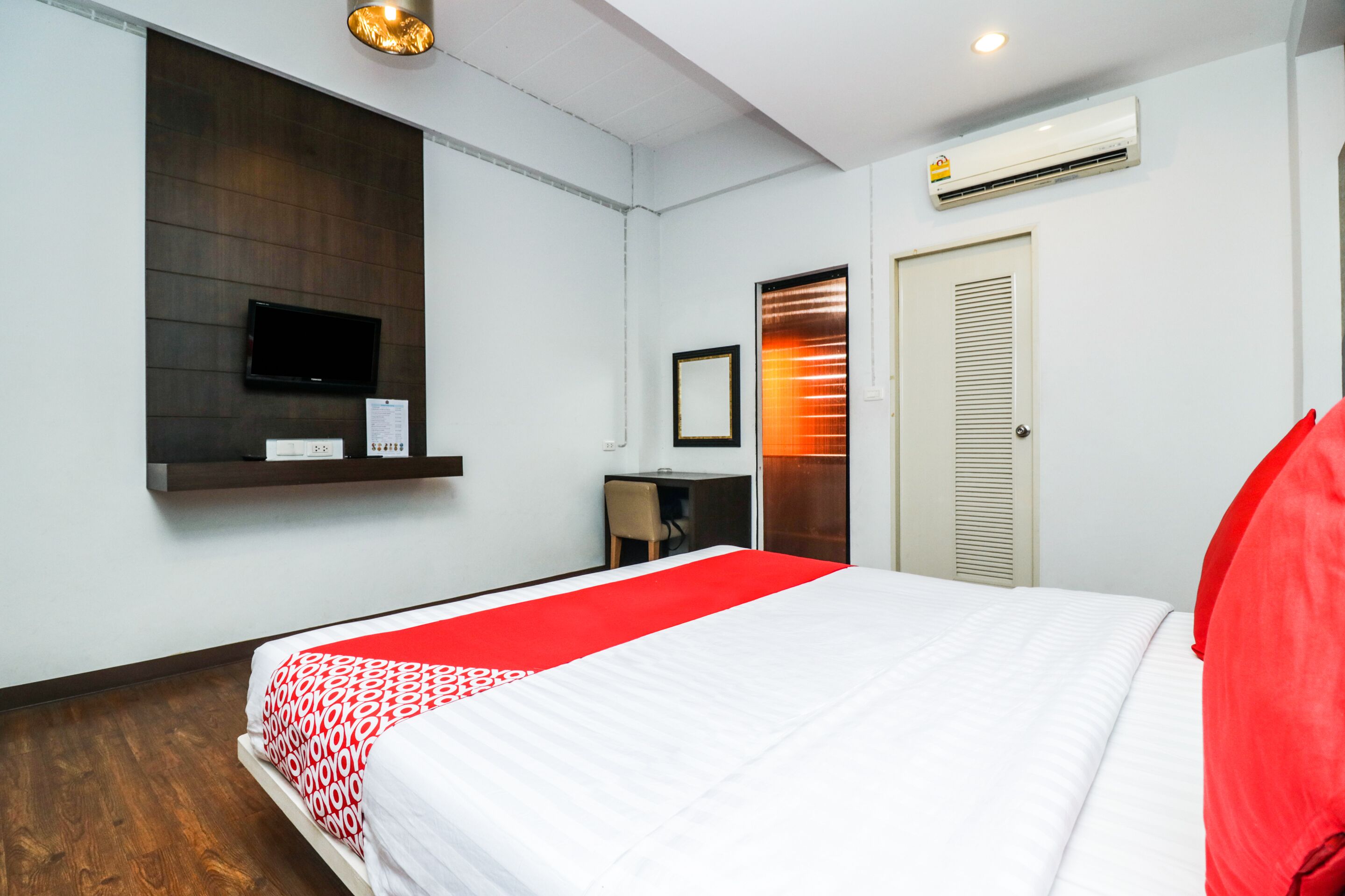 Una habitación de hotel con cama, escritorio, silla, televisor y aire acondicionado.