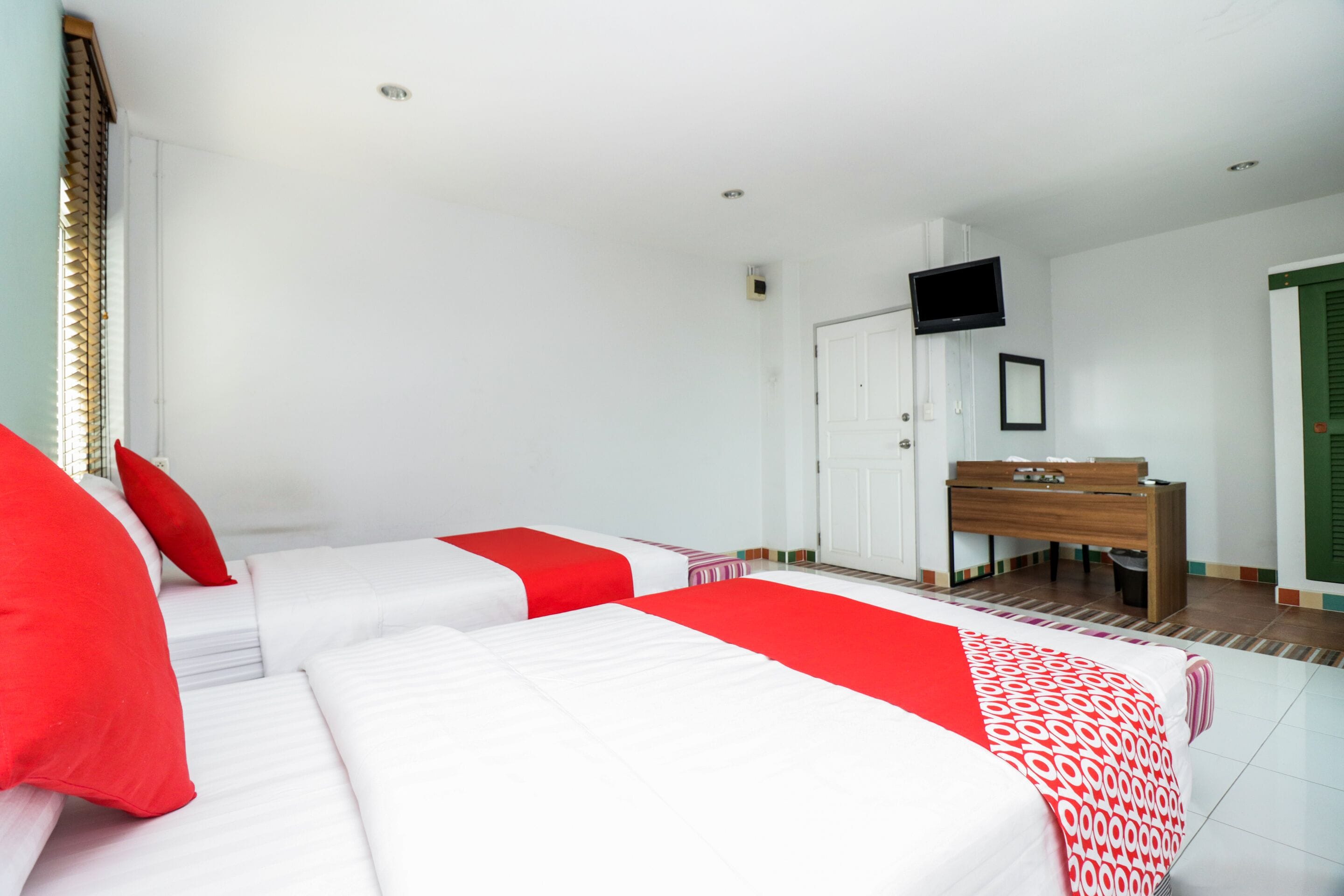 Ein Hotelzimmer mit zwei Betten, einem Schreibtisch, einem Fernseher und einer Tür mit grünem Rollo.