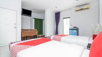 A hotel room with two beds, a desk, a television, and an air conditioning unit.