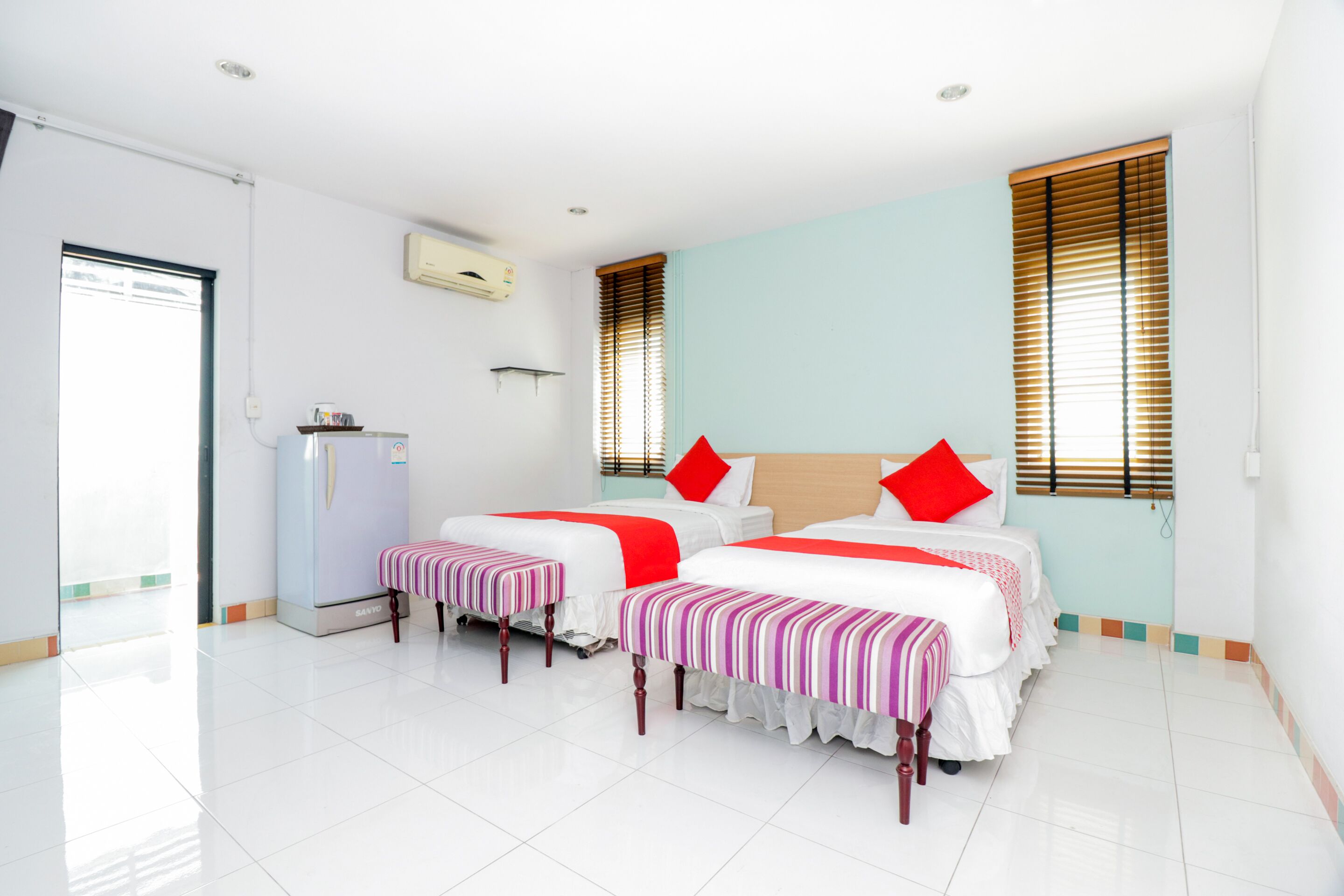 A hotel room with two beds, a refrigerator, and a window with blinds.