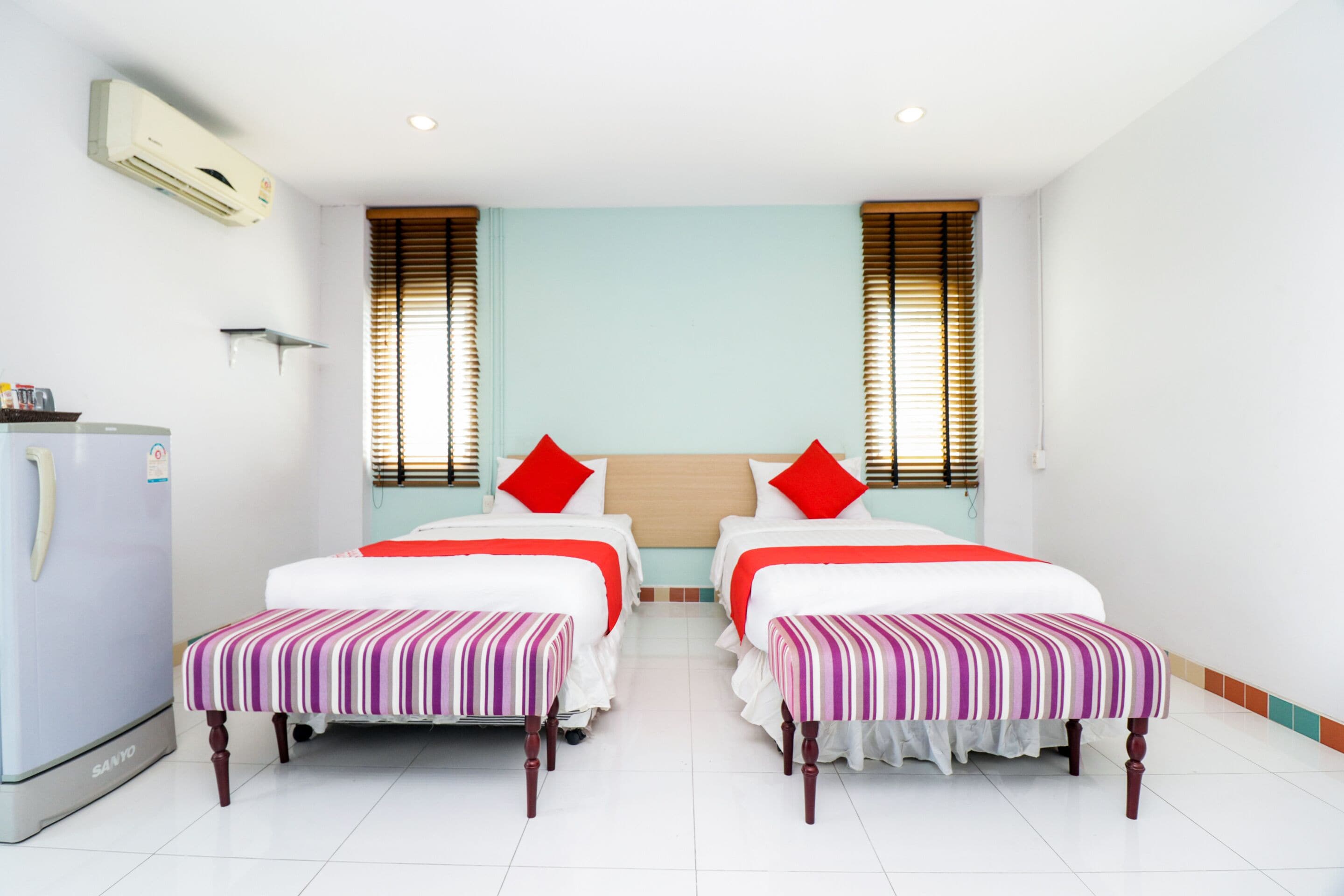 A hotel room with two beds, a refrigerator, and a window with blinds.