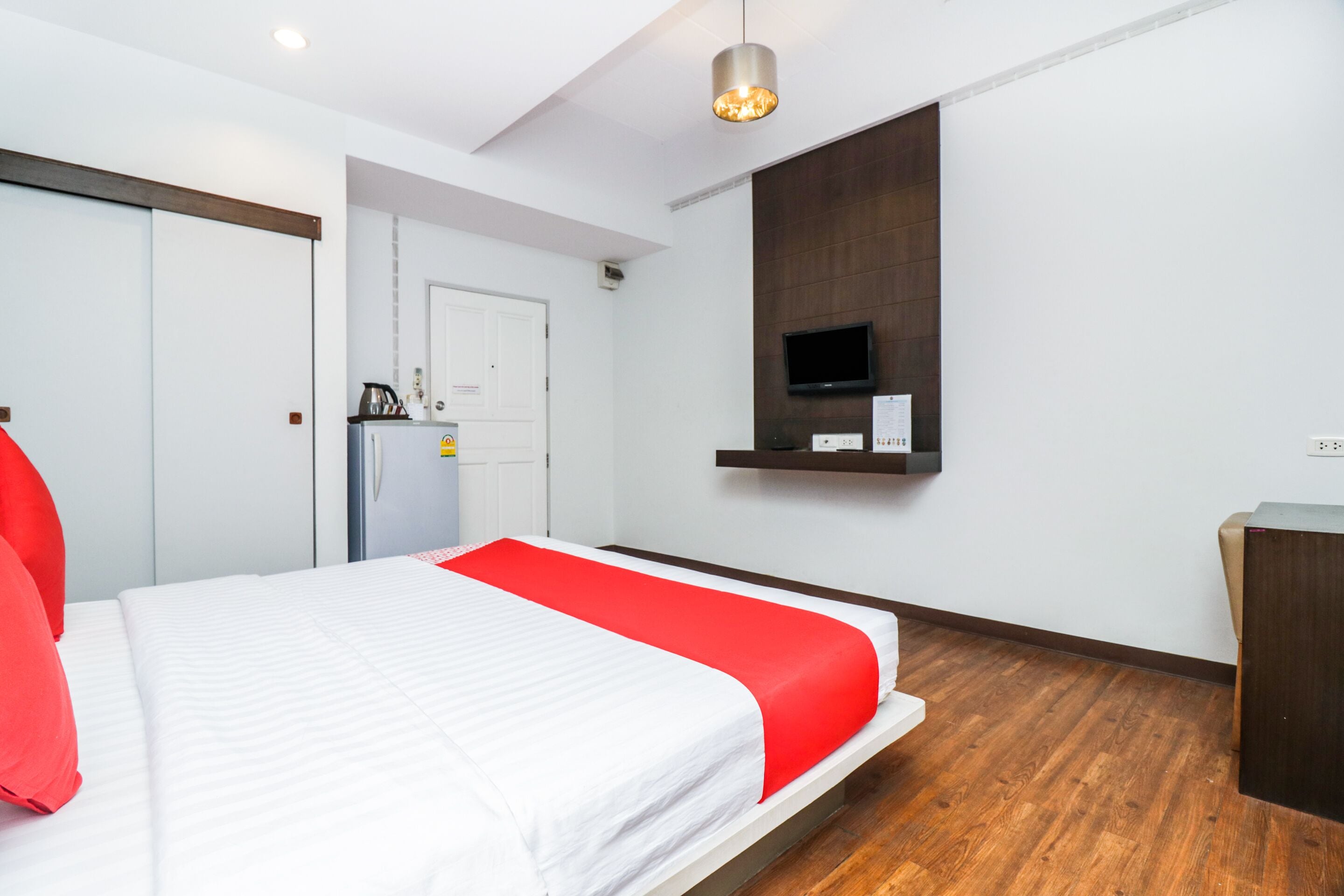 A hotel room with a bed, a TV mounted on the wall, a wooden floor, and a door leading to a kitchenette.