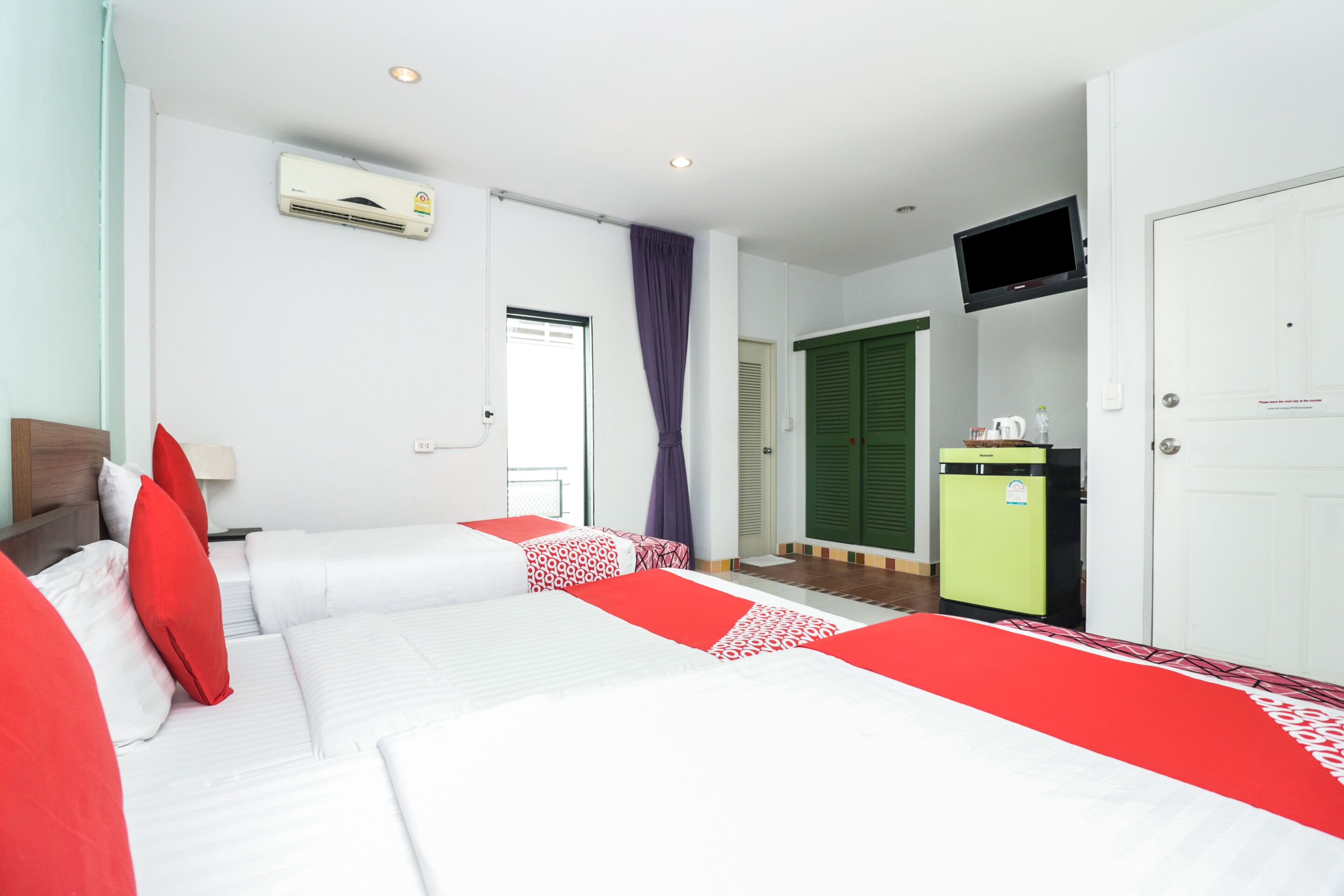 A hotel room with two beds, a television, a minibar, and a door with a sign.