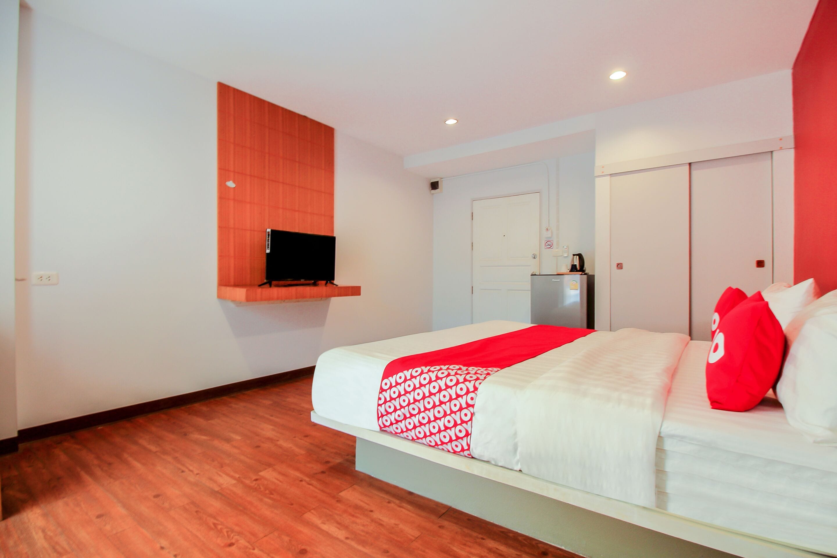 Una habitación de hotel con cama, televisión montada en la pared, armario y una pequeña kitchenette.