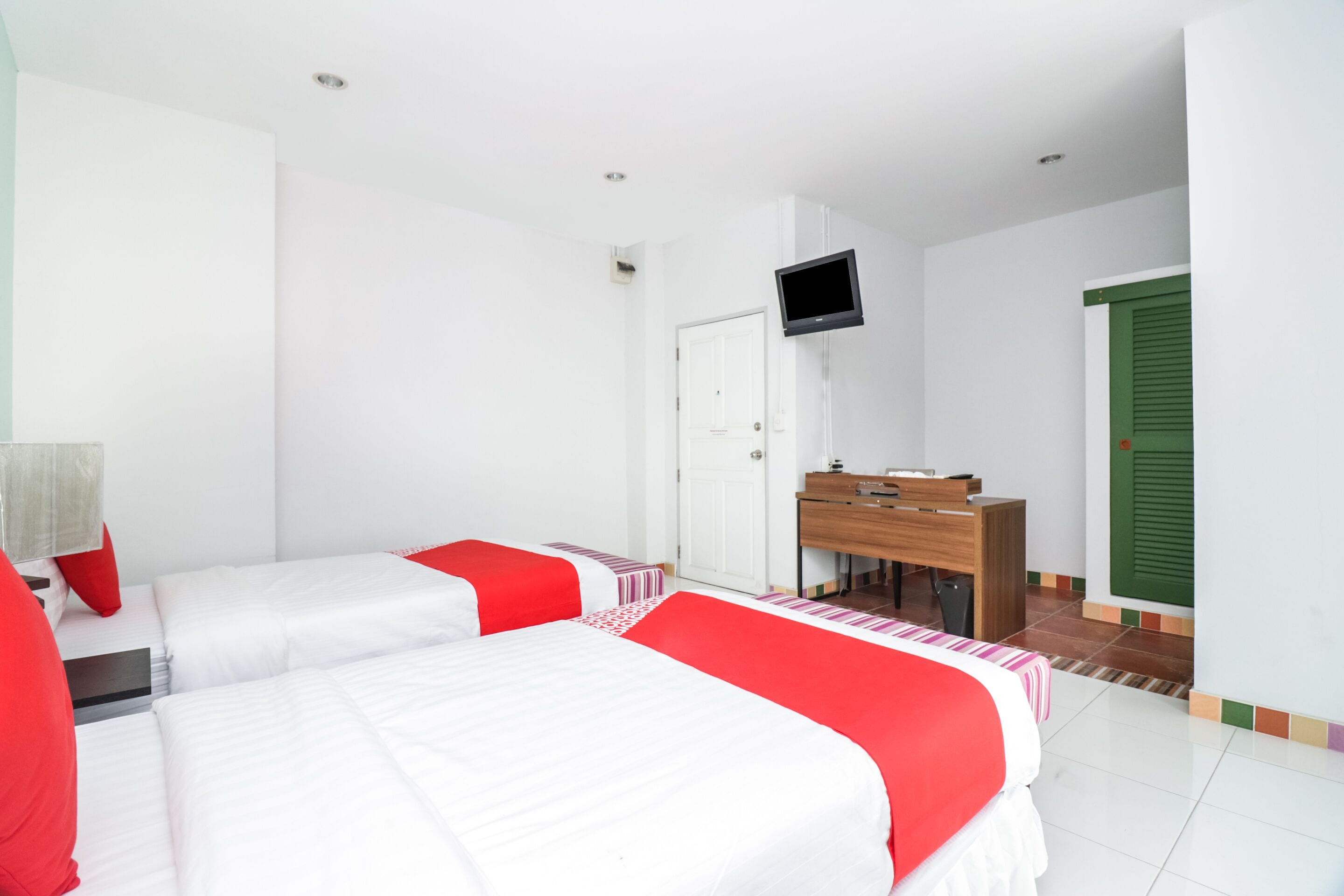 A hotel room with two beds, a desk, a television, and a green door.